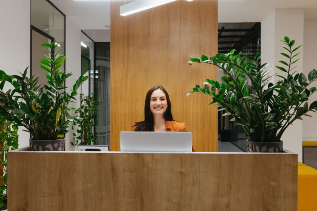 A woman standing behind an office front desk smiling.
