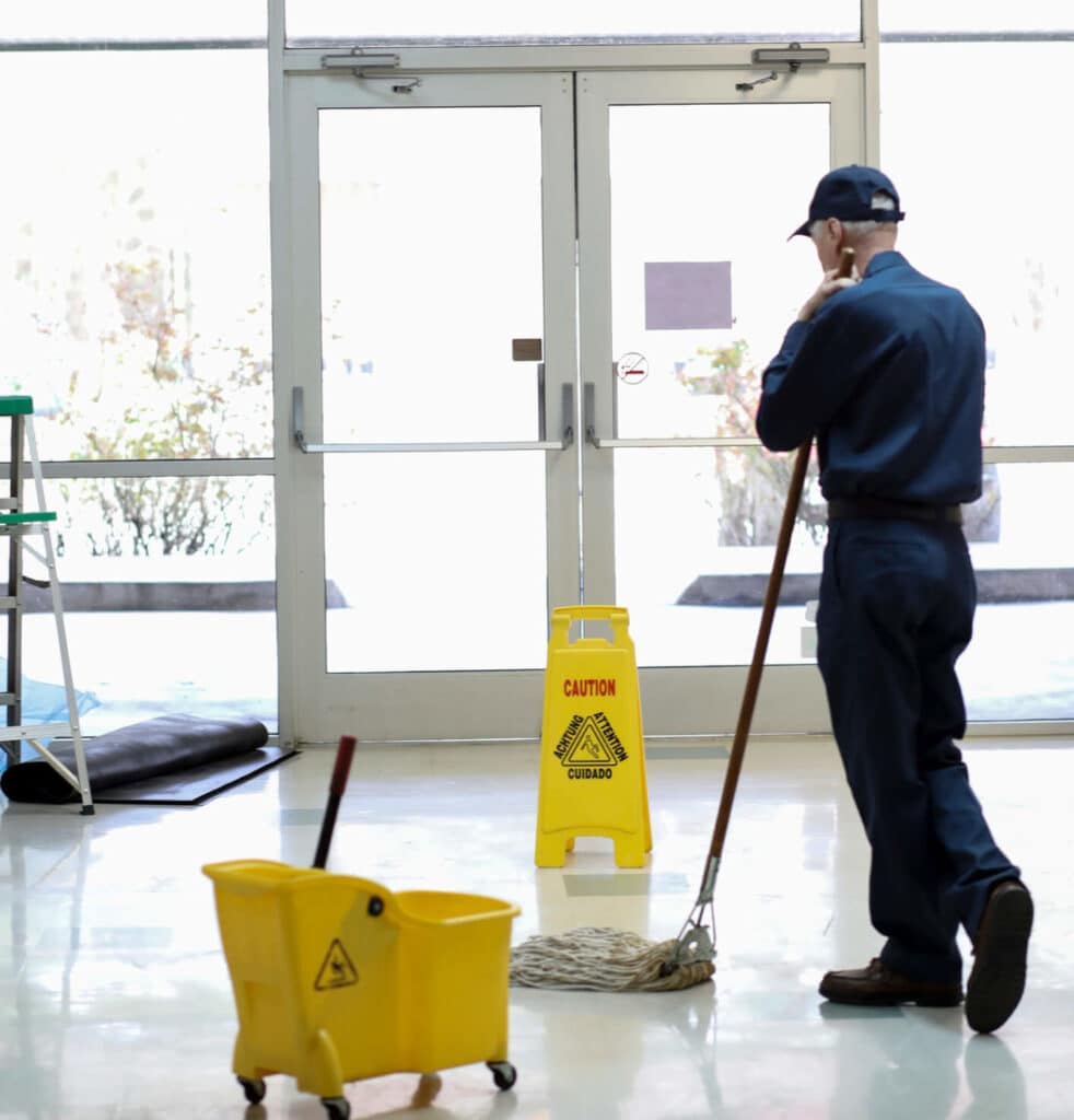 Man in blue coveralls mopping floors in a hallway.