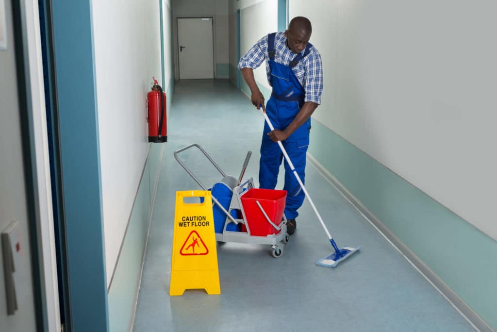 A man in blue coveralls mopping a hallway.