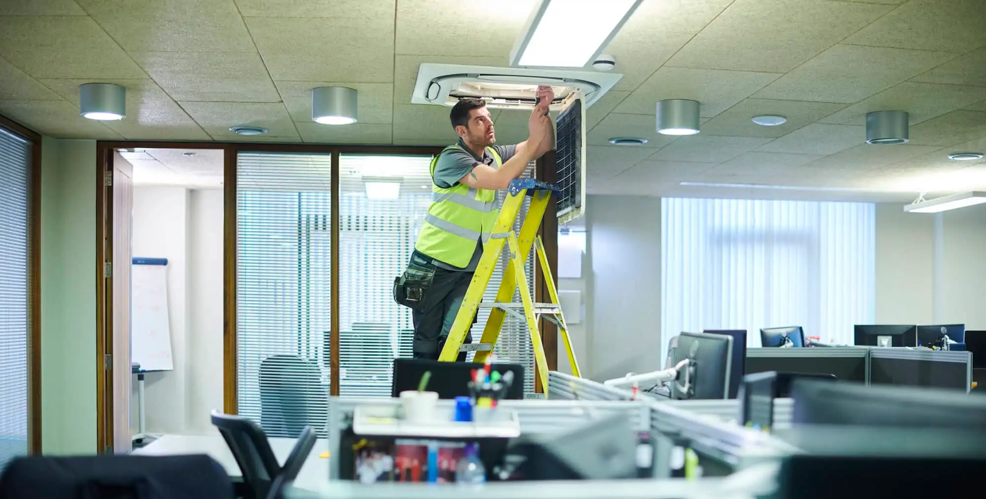 Maintenance technician works on HVAC system in an office.